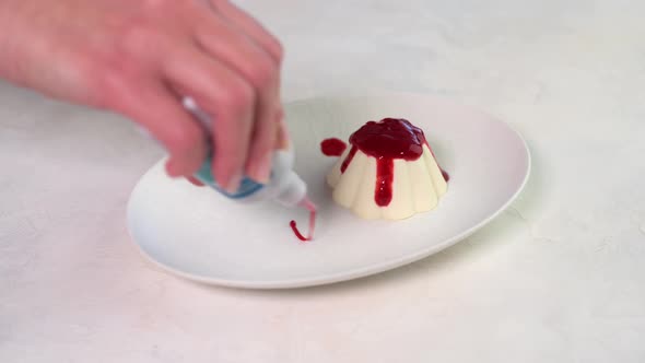 Woman's Hand Draws a Pattern Raspberry Syrup Panna Cotta on White Plate