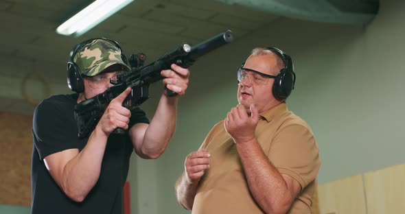 A Man Learns How to Shoot a Rifle at the Shooting Range The Instructor Shows the Trainee the Correct alt