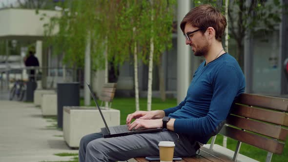 Young business man using laptop while sitting outdoor city park. alt