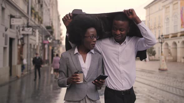 Afro Man and Woman Hiding From Rain Under Jacket alt