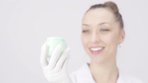 Young Female Researcher Cosmetologist Looking at and Smelling Cosmetics in Jar