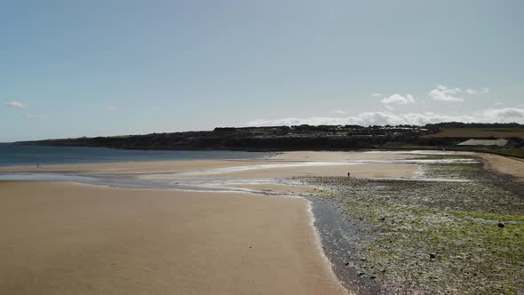 Aerial drone view flying over the beach in St Andrews, Scotland, UK as people walk the beach at low alt