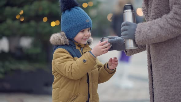 Portrait of Cute Middle Eastern Boy Standing at Christmas Tree in City with Unrecognizable Woman alt