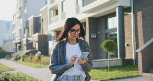 Woman Typing Message at Mobile Phone During Walking at Sunny Windy Weather. Lifestyle, Outdoors alt