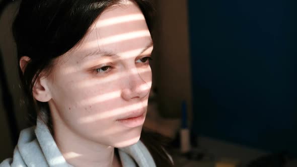 Brunette Woman's Face with Stripes of Light From the Window on Her Face.