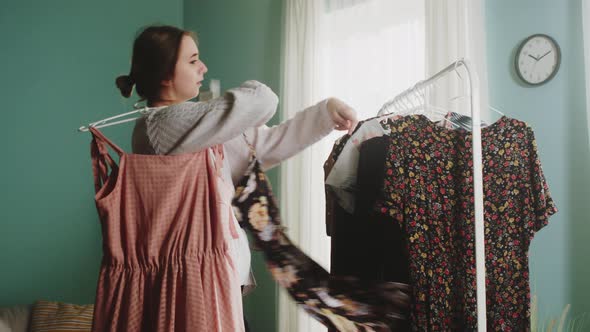 Young Woman with Joyful Emotions Chooses Clothes and Takes the Hanger alt