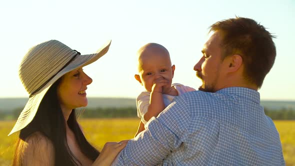 Loving parents hugging and kissing baby in wheat field alt