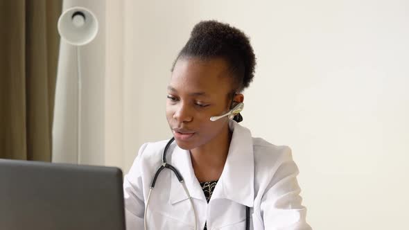 Young African American Woman Doctor with Headset Having Chat or Consultation on Laptop alt
