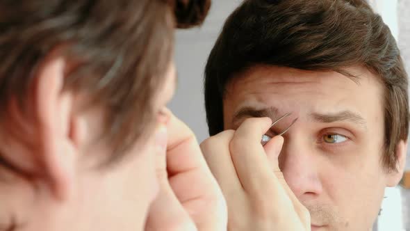 Young Man Plucking His Eyebrows with Tweezers. Styling Eyebrows.
