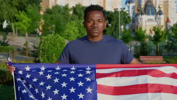Camera Zoom in Patriot AfroAmerican Man Holding American Flag and Looks Camera alt