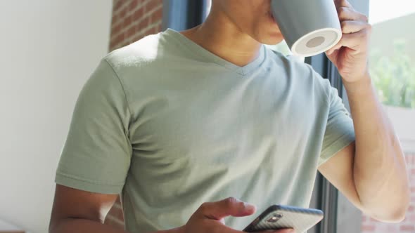 African american man using smartphone and drinking coffee at home alt