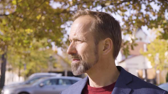 A Middleaged Caucasian Man Looks Seriously at the Camera in a Street in a Small Town in Fall