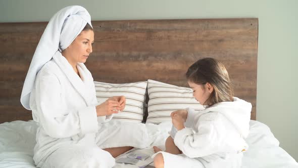 Cute Mother and Daughter in Dressing Gowns Use Face Masks and Patches at Home, Quarantine  alt