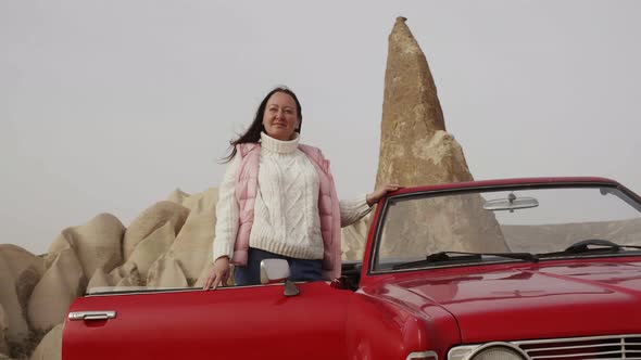 Woman is Standing Near Retro Cabriolet Red Car Among Rocks Admiring View