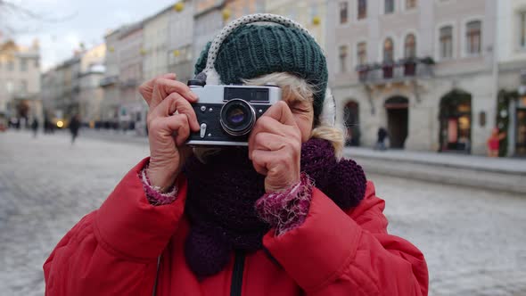 Senior Old Woman Tourist Taking Pictures with Photo Camera Using Retro Device in Winter City Center alt