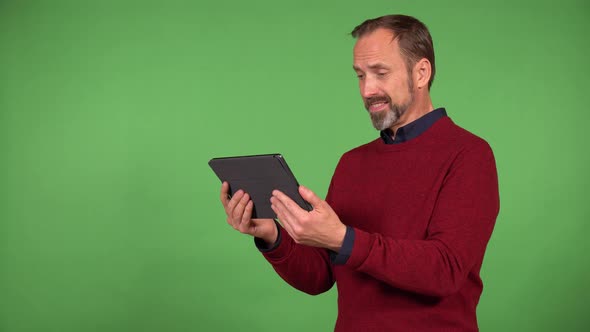 A Middleaged Handsome Caucasian Man Looks at a Tablet with a Smile  Green Screen Background