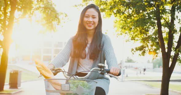 Riding bicycle with basket in city park. Asian happy girl drives vintage bike with cheerful smile