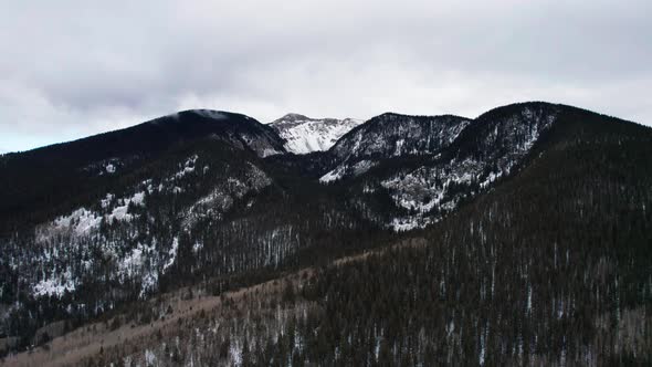 Drone shot pulling back away from a high elevation snow covered mountain alt
