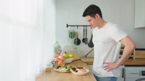 Asian young attractive handsome male eating green salad in kitchen at home. alt