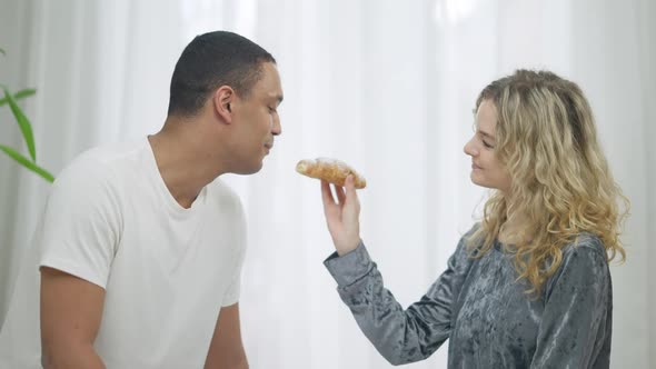 Side View of Loving Slim Beautiful Caucasian Woman Feeding African American Handsome Man with alt