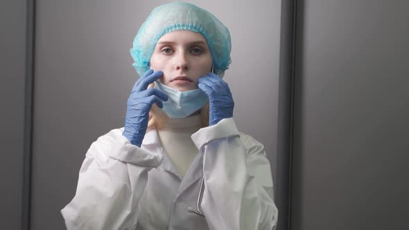A Young Woman Doctor with a Stethoscope Around Her Neck Pulls a Medical Mask Over Her Face and Looks alt