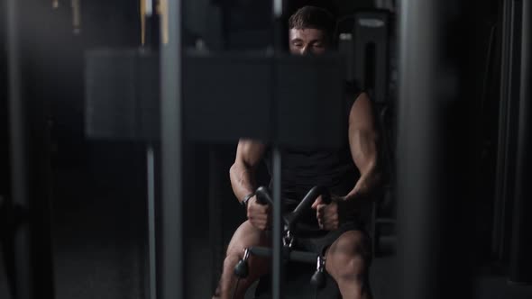 Athletic Man Lifting Blocks on Rowing Machine in the Gym Training on Block Device and Gym Equipment alt