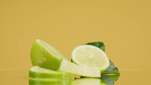 Closeup of Rotating Ripe Limes with Mint Leaves on Yellow Background Making a Cocktail of Citrus alt
