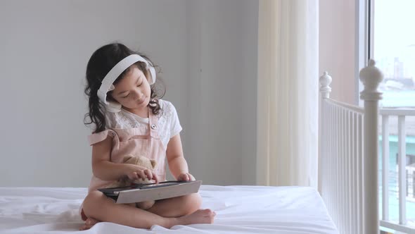 Cute Asian pre-school aged girl listening to music on the bed alt