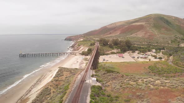 Drone flies over train track along the ocean towards pier in Santa Barbara