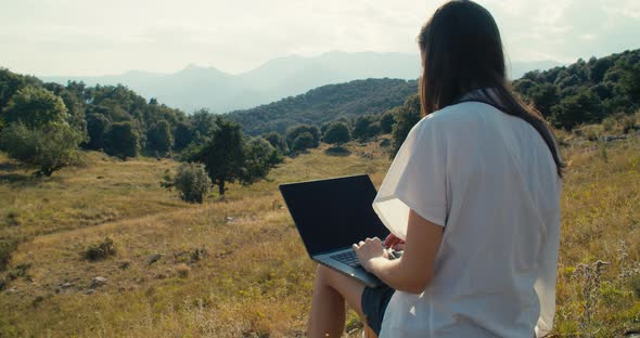 Beautiful Freelance Female Worker Sit on Hill and Type on Notebook Keyboard alt