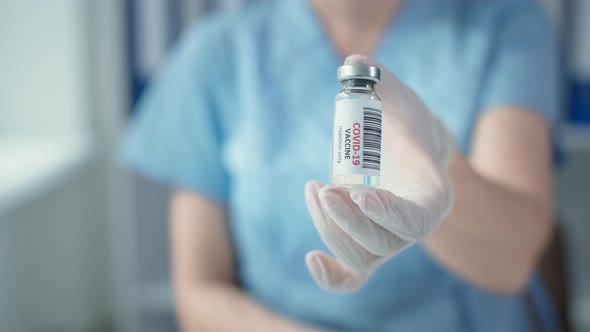 Covid19 Vaccination Medical Worker in a Blue Uniform and Protective Gloves Holds a Vaccine in Glass alt