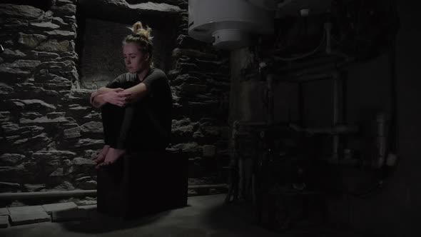 depressed anxious woman sitting in a dark corner of a basement, blinking overhead light