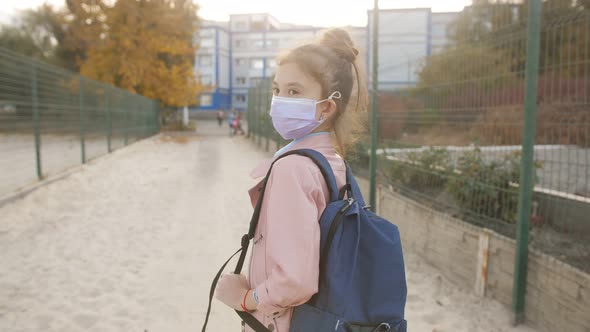 An Elementary School Student Wearing a Medical Protective Mask Walks Towards the School with a alt