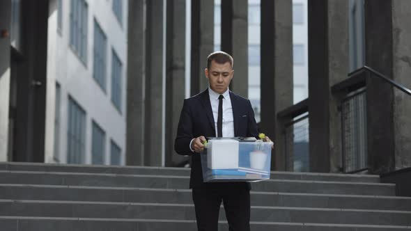 Male Office Worker in Depression With Box of Personal Stuff Walking Outdoor