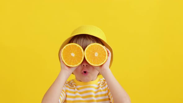 Surprised child holding halves of orange fruit like a sunglasses. Slow motion