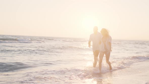 Couple of Young Lovers Holding Hands Walking Along the Beach By the Sea