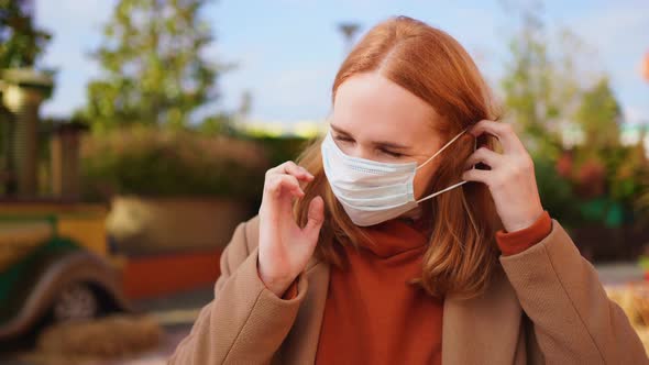 A Woman in a Coat Wears a Protective Medical Disposable Mask While Standing alt
