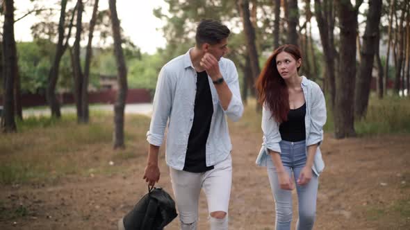 Tired Couple of Hikers Walking with Backpack in Suburban Forest Front View alt