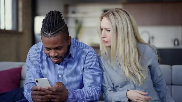 Jealous Caucasian Wife Looking at Smartphone of African American Husband Talking and Gesturing alt