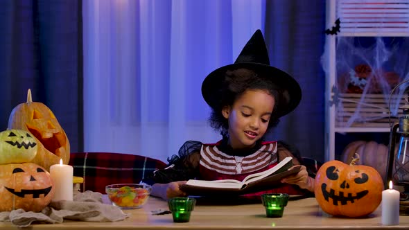 Little African American Girl in Festive Costume Reads Book with Enthusiasm alt