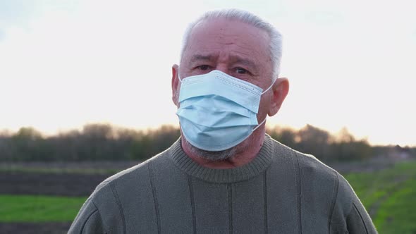 An Elderly Man in a Medical Mask Looks at the Camera alt