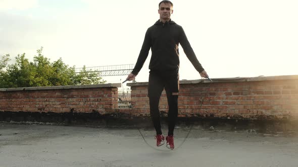Sporty man jumping with rope training outdoors. man uses  skipping rope on roof alt
