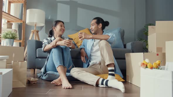 . asian young attractive couple man and woman sit at new home drink coffee relax and talk smile.