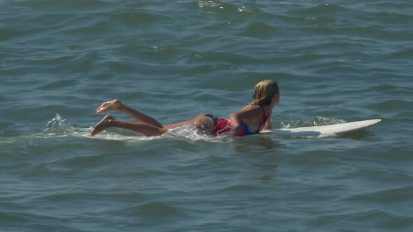 A female surfer paddles on her classic longboard surfboard. alt
