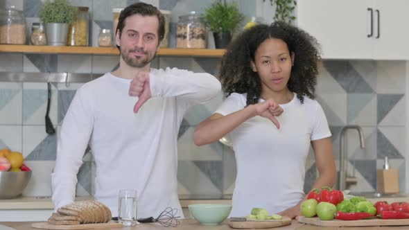 Mixed Race Couple Showing Thumbs Down Sign in Kitchen alt