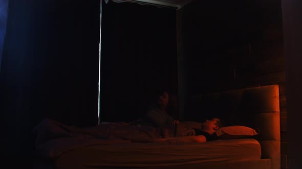 Young Tired Couple Laying on a Bed  Woman Stands Up and Opens Up the Curtains alt