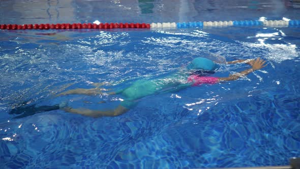 Child Girl in Goggles Swimsuit Cap and Flippers is Training Swimming in Pool alt