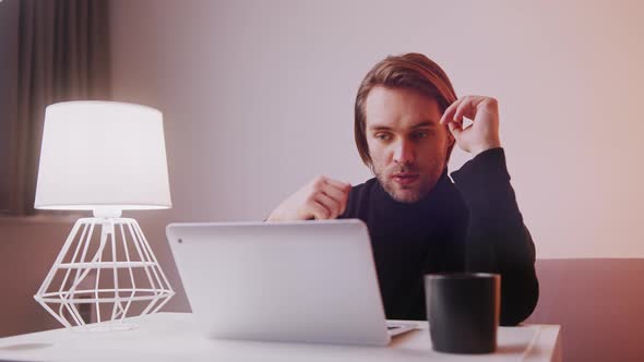 Young Caucasian Man Showing Thumb Up and Thumb Down While Having a Video Call on His Laptop alt