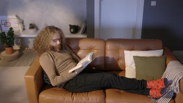 Young Man Reading a Book At Home Sitting on a Couch, Indoor, Real Time