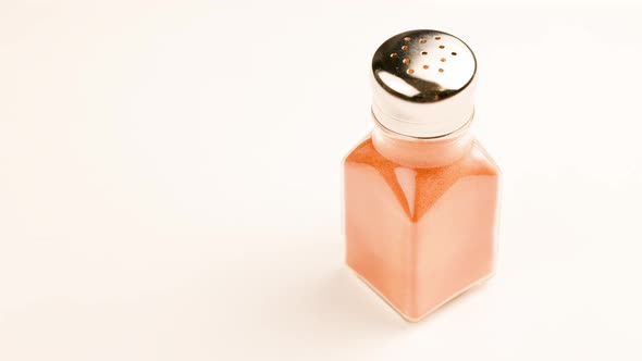 Glass Pepperjar with Stainless Steel Cap Full of Red Paprika Pepper Powder Spinning on White alt